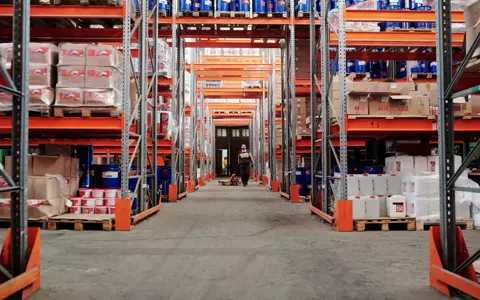 Aisle of a warehouse with stock on tall orange racking
