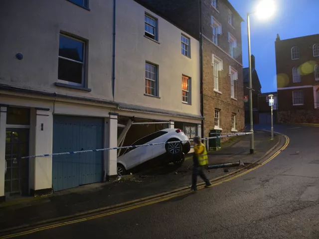 A car that has crashed into the front of a shop on a UK street, with police tape across the pavement